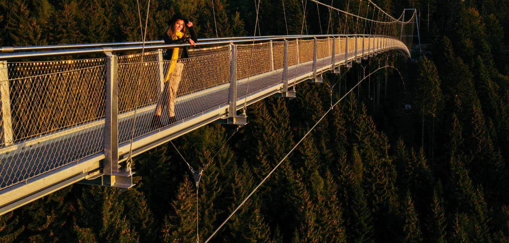 Jeune femme au coucher du soleil sur le pont suspendu WILDLINE
